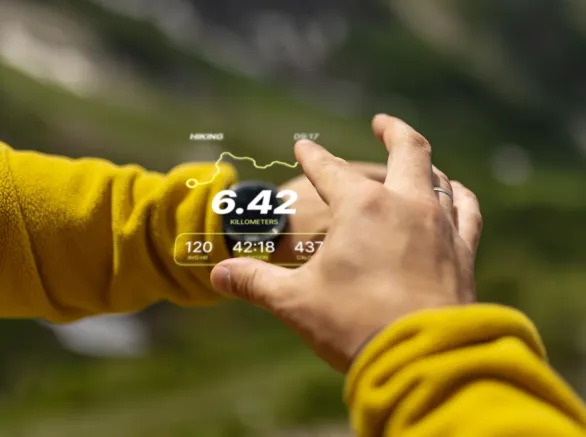Close-up view of a person using augmented reality technology outdoors, displaying hiking statistics. The background features a blurred natural setting, emphasising innovation and adventure in an outdoor environment.